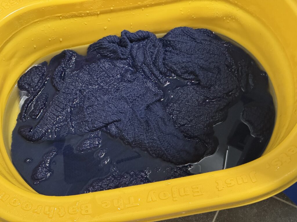 노란색 대야에 물을 받아 네이비 케이블 니트 스웨터를 담가 손세탁 중인 모습.