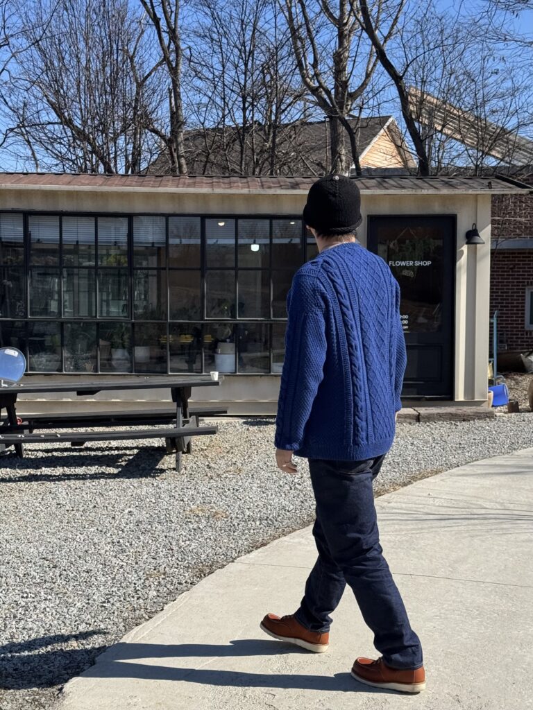 네이비 케이블 니트 스웨터를 입고 건물 앞을 걷는 남성의 전신 모습.