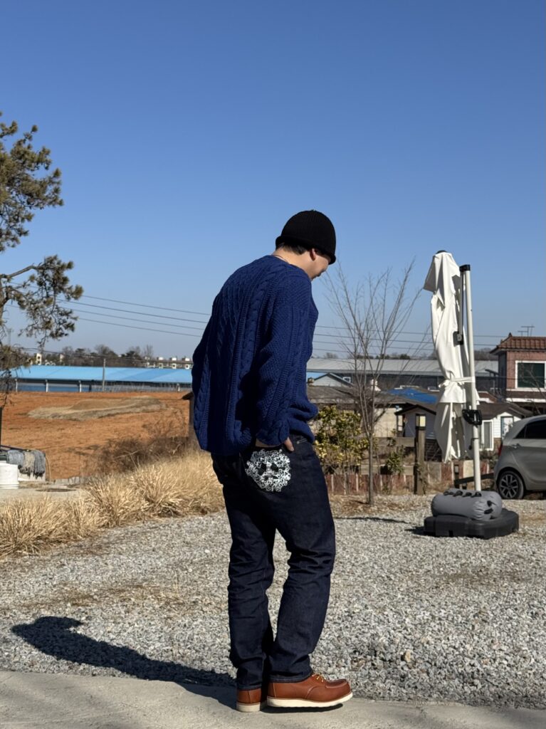 야외에서 네이비 케이블 니트 스웨터를 입은 남성의 뒷모습.