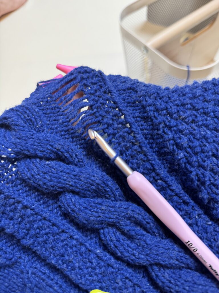 네이비 케이블 니트 편물의 어깨 부분을 코바늘로 한 코씩 주워 정리하는 모습.