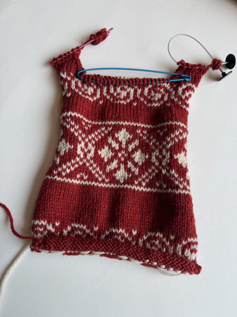 빨간 바탕에 화이트 배색 코위찬 패턴이 완성된 강아지 니트 등판을 평면에 펼쳐 놓은 모습